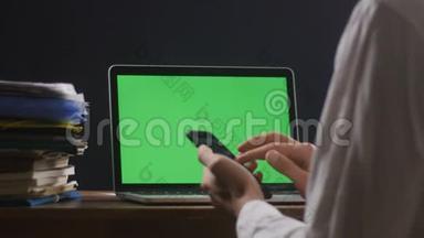 人类正在使用智能手机，他的笔记本电脑上有一个绿色屏幕或一个色度在他的桌面上。 商人在这里工作